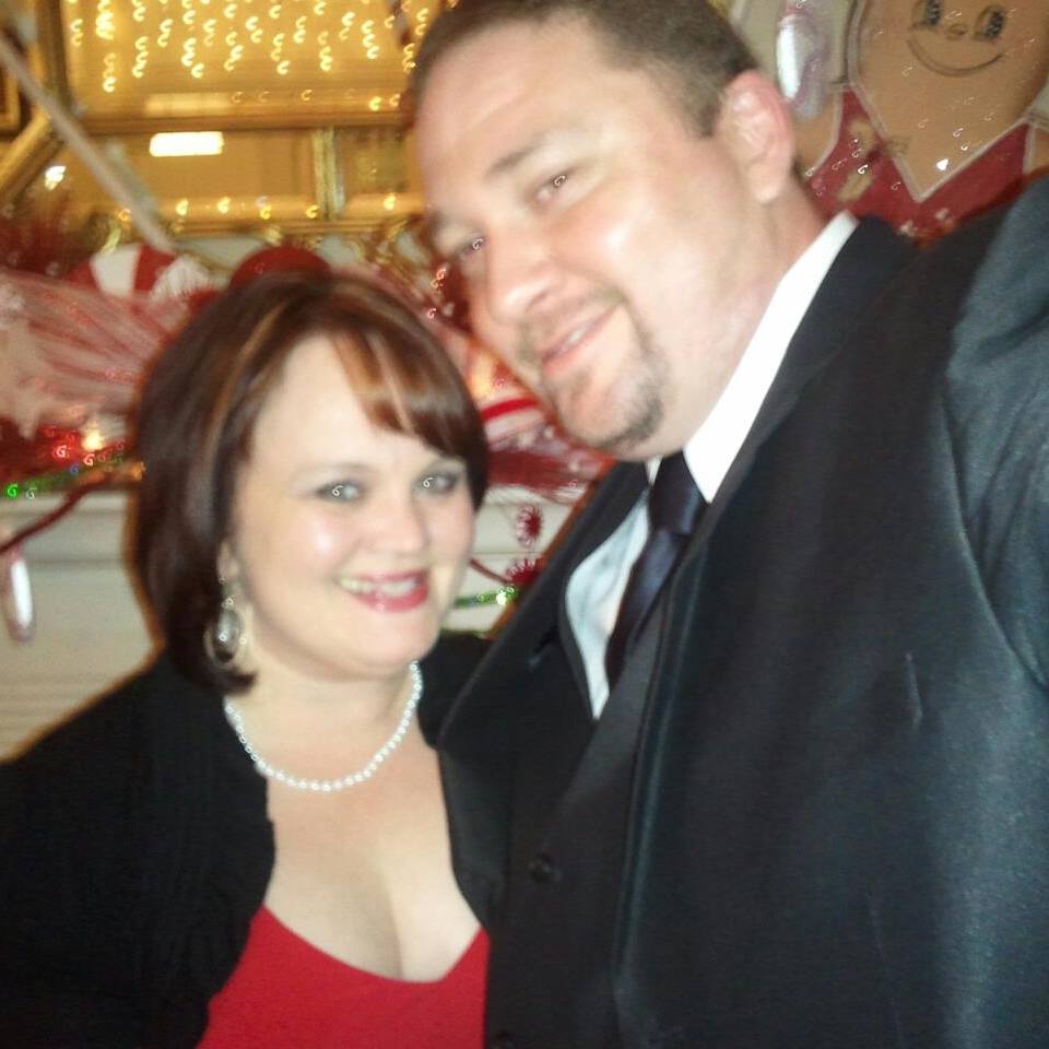 A couple dressed up for a Christmas party in 2011, smiling closely together amid festive holiday decorations during their first Christmas season as a couple.