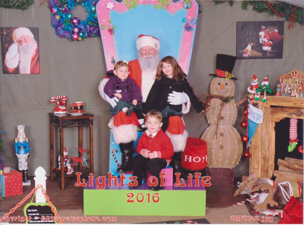 Three grandchildren posing with Santa at the Lights of Life Christmas display in 2016, continuing a family holiday tradition.